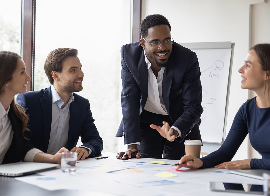 About Our Agency - Inspired Business Professional Standing Up and Speaking to His Colleagues During a Meeting at an Office